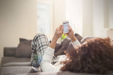 Man relaxing, using smart phone on sofa - CAIF25212