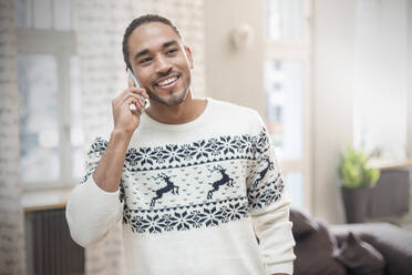 Lächelnder junger Mann im Weihnachtspulli, der mit seinem Handy telefoniert - CAIF25221
