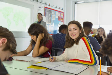 Portrait confident high school girl student taking notes during geography lesson in classroom - CAIF25240