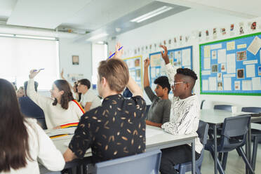 Gymnasiasten mit erhobenen Händen, die während des Unterrichts im Klassenzimmer Fragen stellen - CAIF25242