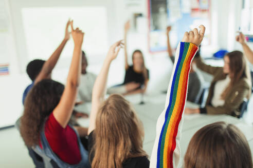 Gymnasiasten mit erhobenen Armen, die im Klassenzimmer Fragen stellen - CAIF25259