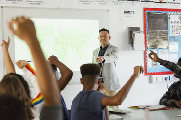 High school teacher leading lesson, calling on students with arms raised in classroom - CAIF25271