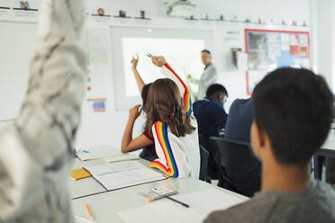 High school students with hands raised during lesson in classroom - CAIF25276