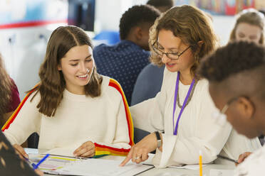 Female high school teacher helping girl student with homework in classroom - CAIF25289