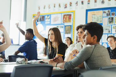 Gymnasiasten mit erhobenen Händen, die während des Unterrichts im Klassenzimmer Fragen stellen - CAIF25295