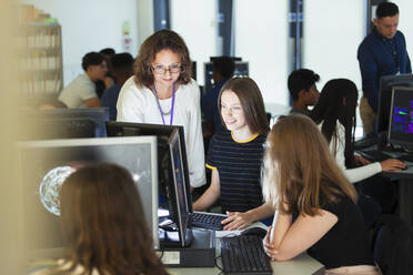 Female junior high teacher helping girl student at computer in computer lab - CAIF25299