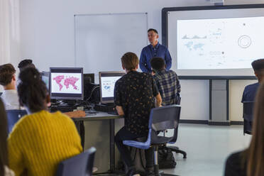 Schüler der Mittelstufe an Computern, die den Lehrer auf der Projektionsfläche im Klassenzimmer beobachten - CAIF25300