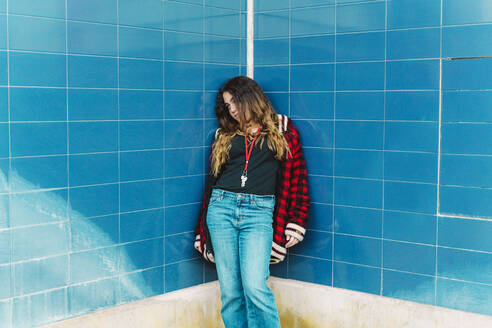 Teenage girl leaning at tiled blue wall outdoors - ERRF02962