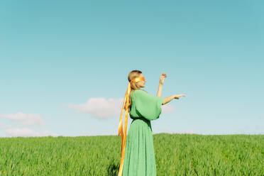 Junge Frau mit verbundenen Augen und grünem Kleid steht auf einem Feld - ERRF02976