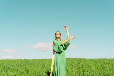 Junge Frau mit verbundenen Augen und grünem Kleid steht auf einem Feld - ERRF02977