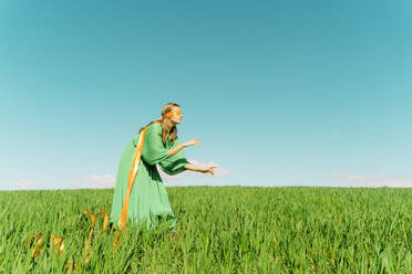 Junge Frau mit verbundenen Augen und grünem Kleid steht auf einem Feld - ERRF02982