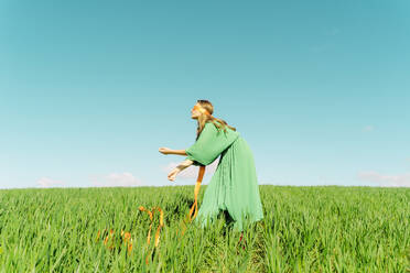 Junge Frau mit verbundenen Augen und grünem Kleid steht auf einem Feld - ERRF02984