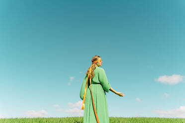 Junge Frau mit verbundenen Augen und grünem Kleid steht auf einem Feld - ERRF02998