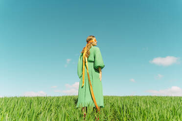 Junge Frau mit verbundenen Augen und grünem Kleid steht auf einem Feld - ERRF02999