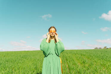 Junge Frau mit verbundenen Augen und grünem Kleid steht auf einem Feld - ERRF03003