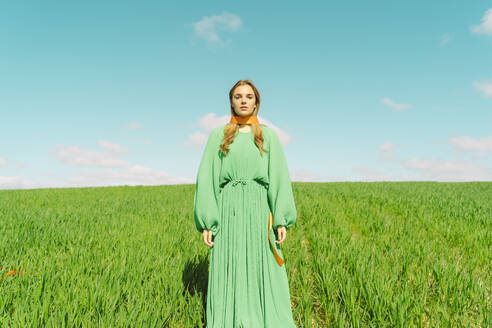 Porträt einer jungen Frau in grünem Kleid, die mit einem Band um den Hals in einem Feld steht - ERRF03005