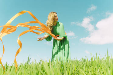 Junge Frau in grünem Kleid steht auf einem Feld mit wehenden Bändern - ERRF03026