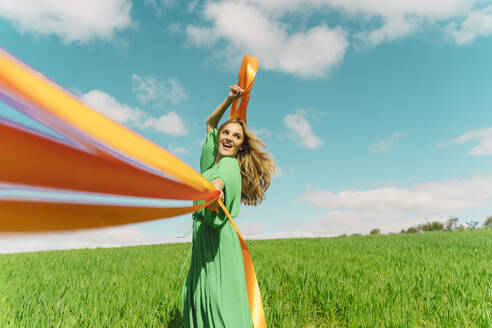 Glückliche junge Frau in einem grünen Kleid auf einem Feld mit wehenden Bändern - ERRF03038