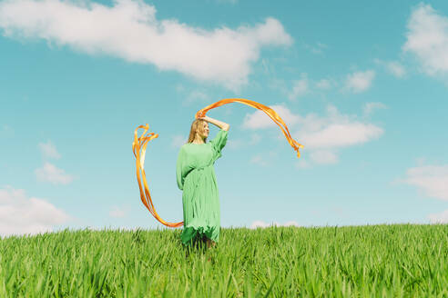 Glückliche junge Frau in einem grünen Kleid auf einem Feld mit wehenden Bändern - ERRF03041