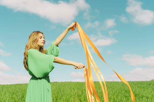 Junge Frau in grünem Kleid steht auf einem Feld mit wehenden Bändern - ERRF03045