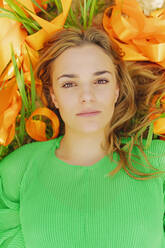 Portrait of young woman lying in a field with orange ribbons - ERRF03055