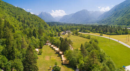 Luftaufnahme eines Campingplatzes inmitten eines Kiefernwaldes mit Bergen im Hintergrund im Soca-Tal, Bovec, Slowenien. - AAEF07956