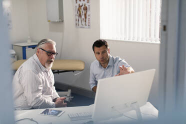 Männlicher Arzt trifft sich mit einem älteren Patienten am Computer in einer Arztpraxis - CAIF25373