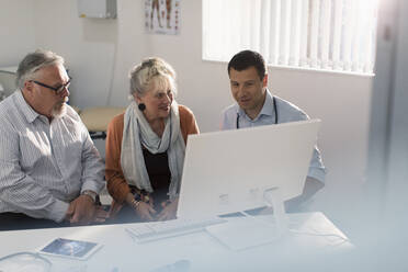 Doctor meeting with senior couple at computer in doctors office - CAIF25374
