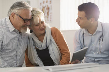 Male doctor with digital tablet meeting with senior couple in doctors office - CAIF25379