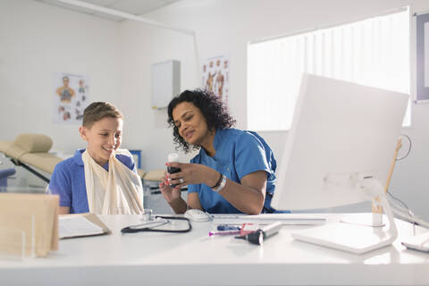 Kinderärztin verschreibt Medikamente für einen Jungen mit Arm in einer Schlinge in einer Arztpraxis, lizenzfreies Stockfoto