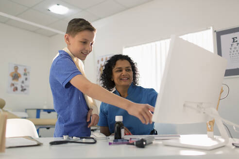 Female pediatrician and boy patient using computer in doctors office - CAIF25423