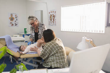 Eine Kinderärztin untersucht ein kleines Mädchen auf dem Tisch im Untersuchungsraum - CAIF25430