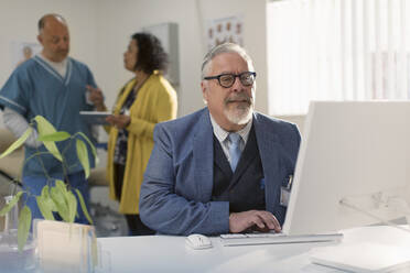 Male doctor working at computer in doctors office - CAIF25435