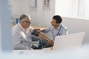 Male doctor checking blood pressure of senior patient in doctors office - CAIF25438