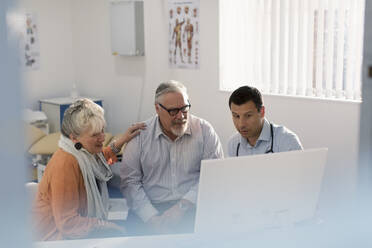 Doctor meeting with senior couple at computer in doctors office - CAIF25439