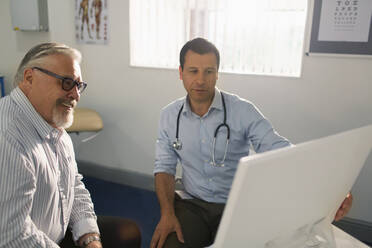 Männlicher Arzt trifft sich mit einem älteren Patienten am Computer in einer Arztpraxis - CAIF25440