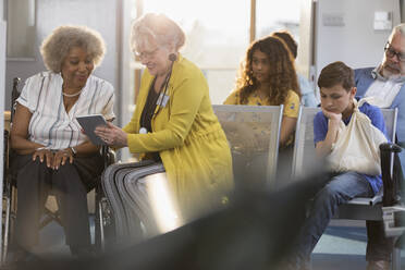 Female doctor with digital tablet talking to patient in clinic lobby - CAIF25445