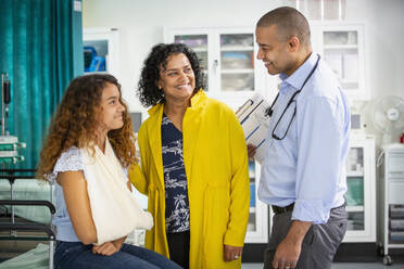 Male pediatrician talking to girl patient with arm in sling in examination room - CAIF25453