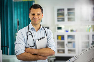 Portrait confident male doctor with digital tablet in hospital room - CAIF25457