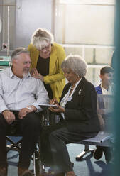 Doctor with digital tablet talking to couple in clinic lobby - CAIF25461