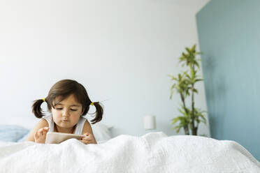 Portrait of little girl lying on bed using at smartphone - VABF02717