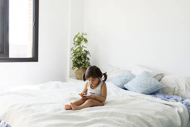 Little girl in underwear sitting on bed using smartphone - VABF02720