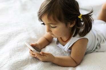 Little girl lying on bed playing with smartphone stock photo