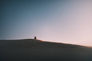 Distant View Of Man Sitting On Sand Dune gegen klaren Himmel - EYF02168