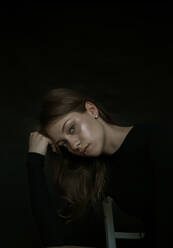 Porträt der schönen jungen Frau sitzend gegen schwarzen Hintergrund - EYF02202