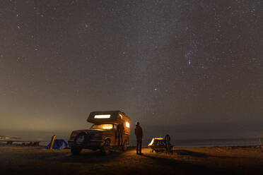 Person standing next to camper-van parked near Jordan River, British Columbia, Canada at night. - CUF54941