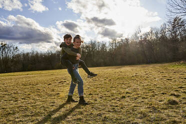 Happy girl carrying brother piggyback on a meadow - AUF00271