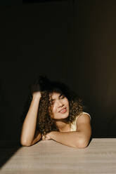 Porträt einer attraktiven jungen Frau, die sich auf einen Tisch im Sonnenlicht stützt - TCEF00401