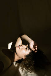 Porträt einer attraktiven jungen Frau im Bett liegend im Sonnenlicht - TCEF00404