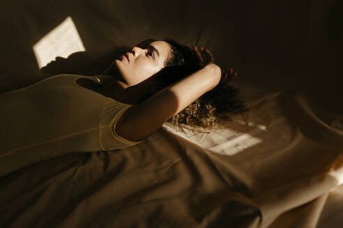 Portrait of attractive young woman lying in bed in sunlight - TCEF00406